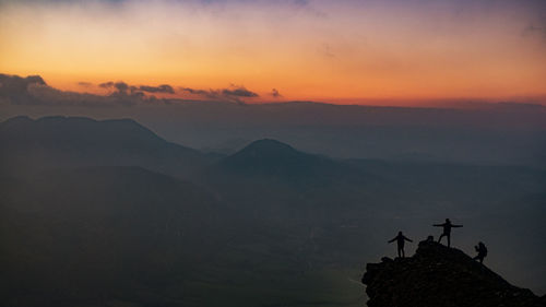 Silhouette people on mountain against sky during sunset