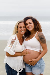 Mom posing with pregnant daughter on beach
