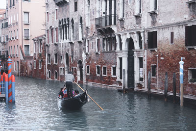 Rear view of people on boats in canal amidst buildings in city