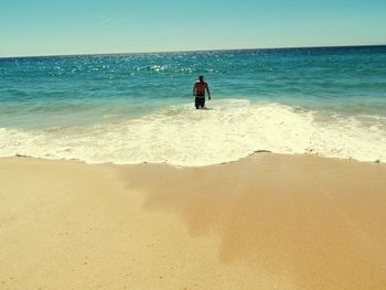 Rear view of shirtless man standing in sea against clear sky during summer
