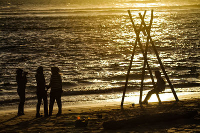 Silhouette people on swing at beach during sunset