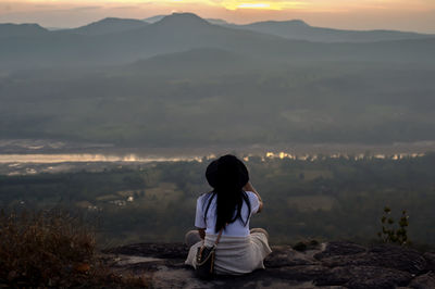 Rear view of woman sitting on mountain against sky