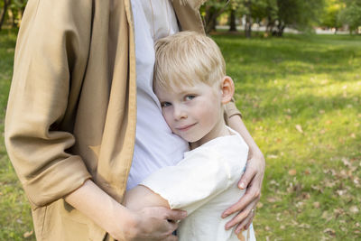 Little smiling caucasian 7 yo boy hugs his mother tight in park. mom's support and care. summer time