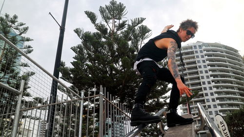 Handsome tattooed guy with sun glasses and spiky hair surfing the staircase hand rails in australia.