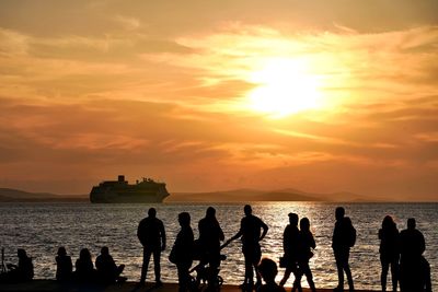 Silhouette people on beach against sky during sunset