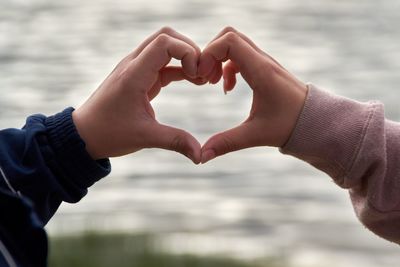 Cropped hands of couple making heart shape against sea