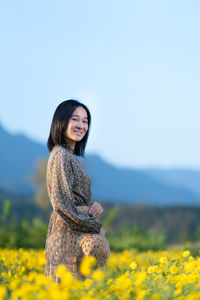 Portrait of woman standing by yellow flower on field