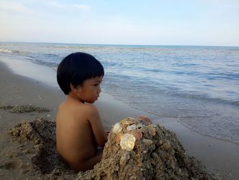 Boy looking at sea shore against sky