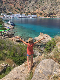 Rear view of woman standing on rock by lake