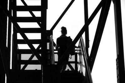 Rear view of silhouette man standing on railing against sky