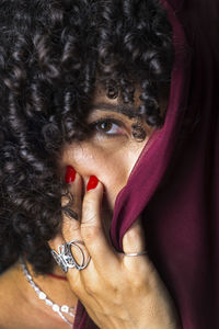 Close-up portrait of woman with red transparent cloth on her face against black background. 