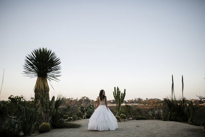 Teenage girl wearing gown while standing in garden against clear sky during quinceanera at sunset