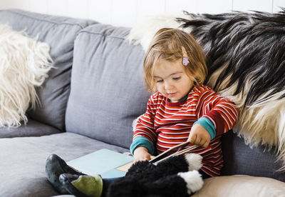 Girl reading book while sitting on sofa at home