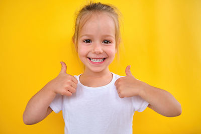 Portrait of smiling girl gesturing against yellow wall