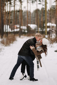 A happy couple in love in winter clothes hugging together walking in a snowy forest on an weekend