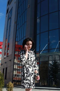 Fashionable young woman wearing floral patterned dress standing against building in city