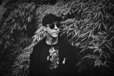 Young man wearing sunglasses standing against plants