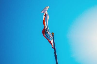 Low angle view of flag waving against clear blue sky