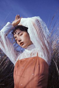 Young woman with eyes closed standing by plants against sky