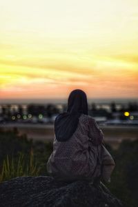 Woman sitting on land against sky during sunset