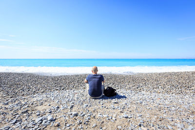 Rear view of woman sitting on beach against sky