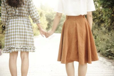 Midsection of women holding hands on road