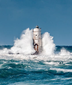 Lighthouse by sea against clear sky