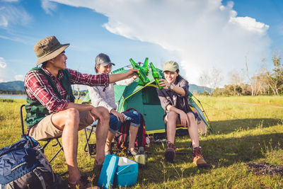 Friends toasting beer bottles while camping on field 