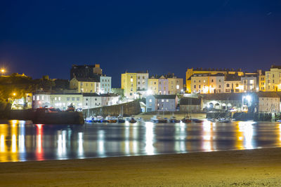 Illuminated buildings by sea against clear blue sky at night