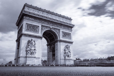 Low angle view of arc de triomphe against cloudy sky