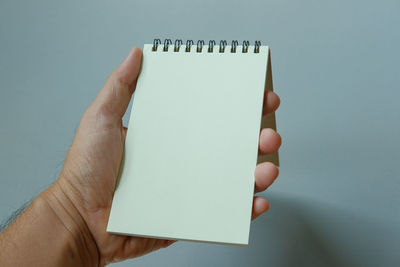 Close-up of hand holding blank notepad against gray background