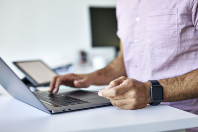 Midsection of businessman with credit card doing online shopping over laptop computer on desk in office