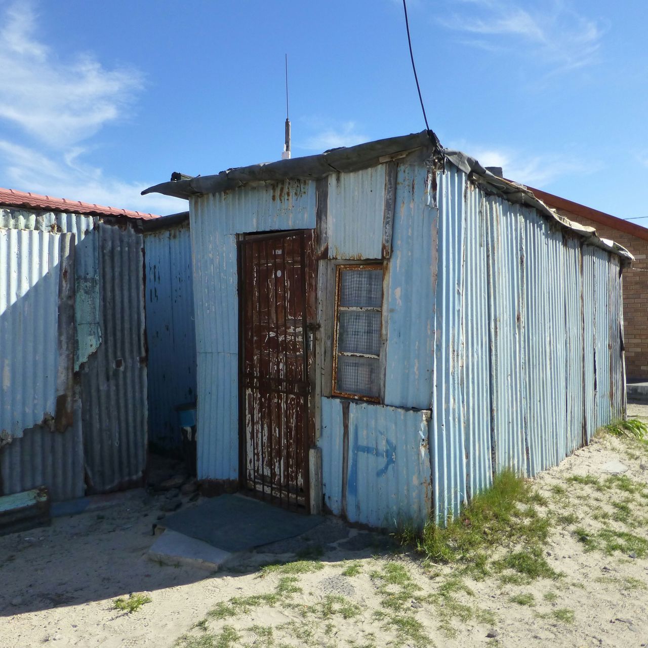 architecture, built structure, building exterior, house, sky, blue, door, closed, residential structure, day, no people, outdoors, sunlight, old, fence, abandoned, safety, protection, grass, window