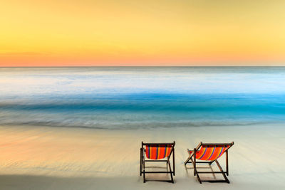 Deck chairs on beach against sky during sunset