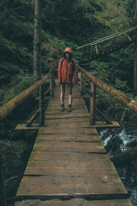 Rear view of man walking on footbridge in forest