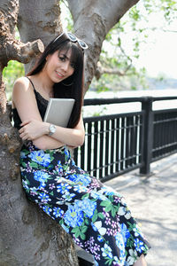 Beautiful young woman using mobile phone while sitting on tree