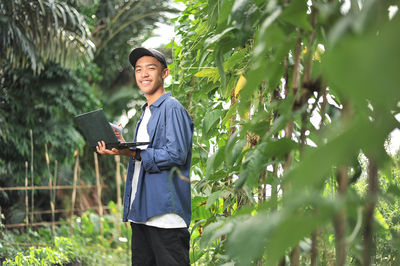 Young asian farmer man holding laptop at the garden