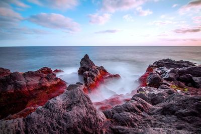 Scenic view of rock formations by sea against cloudy sky