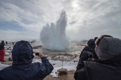 Rear view of tourist taking picture of geyser