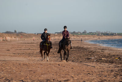 Men riding horse on field against clear sky