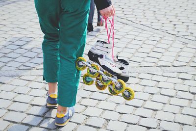 Low section of woman holding skates while standing on footpath