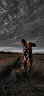 Man holding hoe standing on field against sky