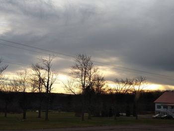 Bare trees on field against sky during sunset