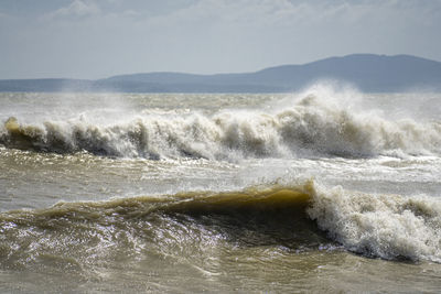 Waves rushing towards shore against sky