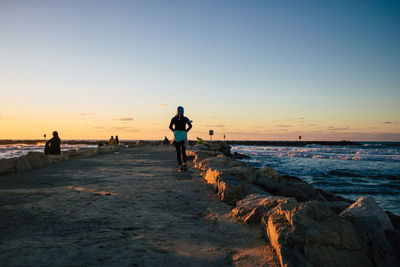 People on beach against clear sky during sunset