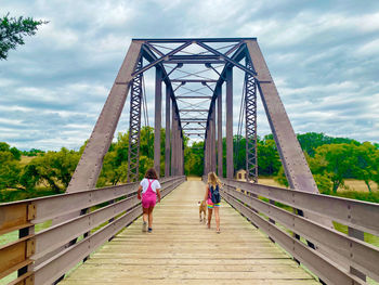 Rear view of women walking on footbridge against cloudy sky