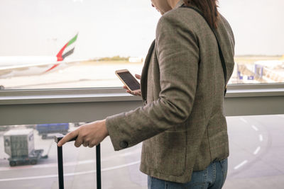 Woman at airport using smartphone with airplane in the background