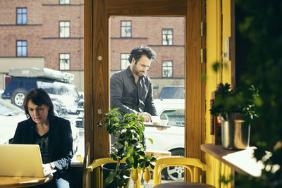 Customer using laptop with waiter seen through glass door at cafe