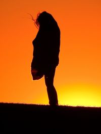Silhouette person on field against orange sky