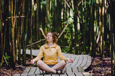 Young woman sitting in meditation pose, relaxing among the bamboo tress.